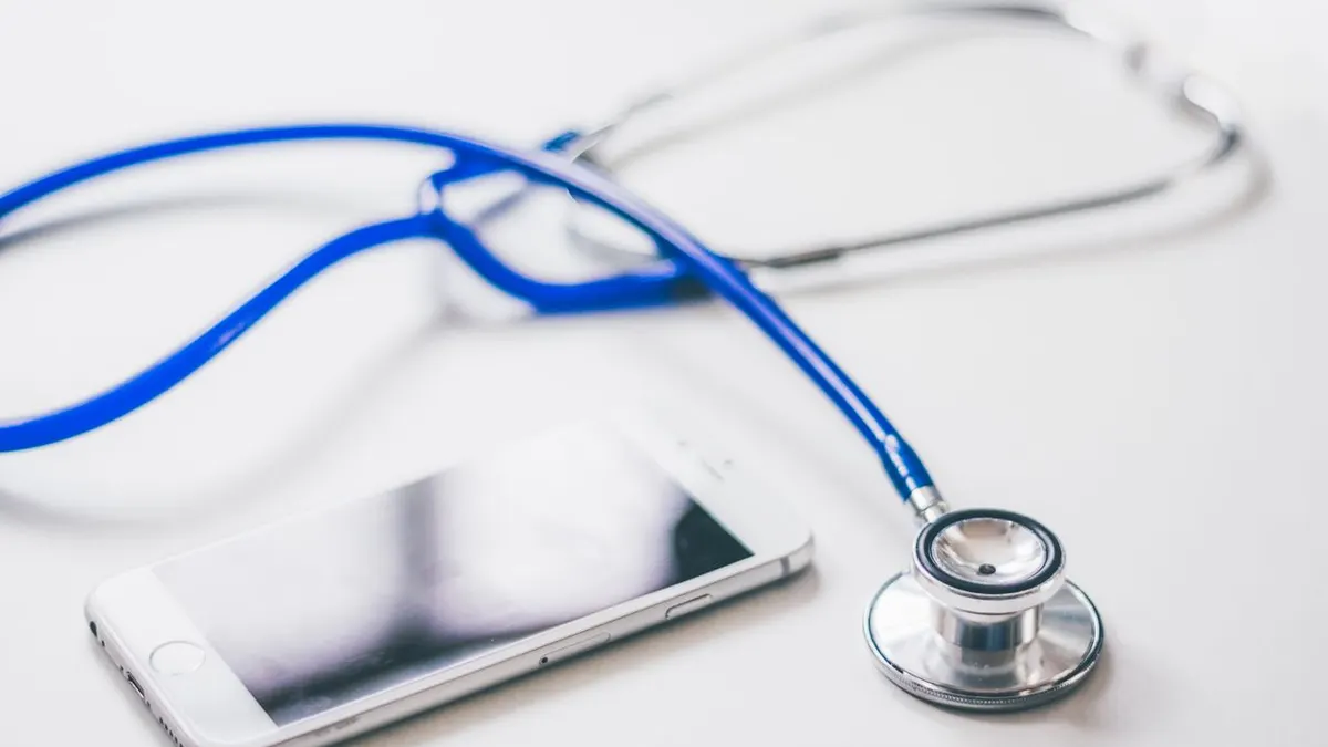 Un smartphone y un estetoscopio azul sobre una superficie blanca y limpia, enfatizando la atención médica moderna.