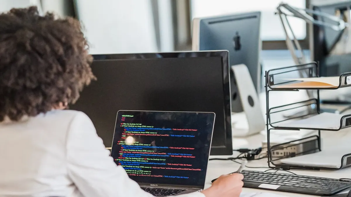 Mujer de negocios enfocada programando en su escritorio en un entorno de oficina moderna, demostrando concentración y
