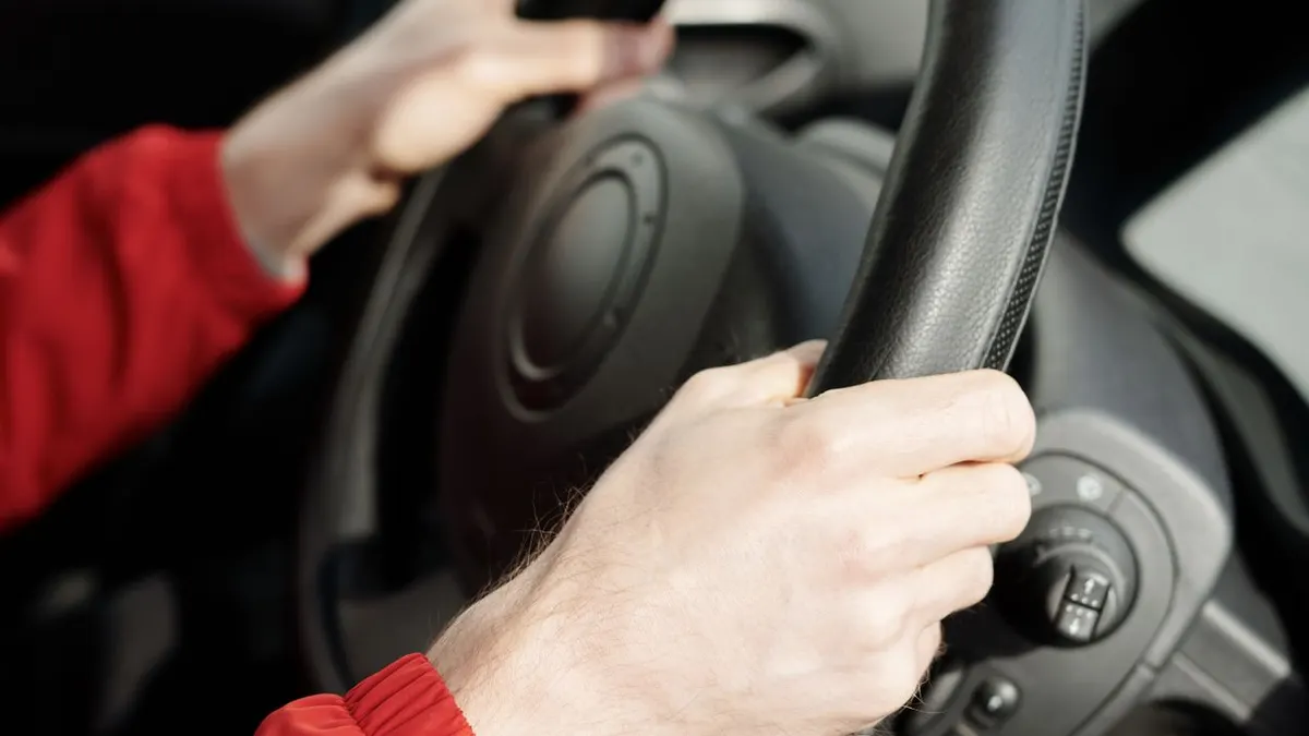 Las manos de una persona agarrando el volante dentro de un vehículo, enfatizando la conducción segura.