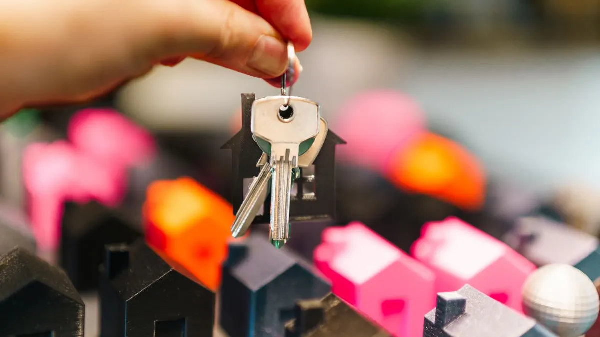 Casas en miniatura de colores y una mano sosteniendo llaves que representan decisiones inmobiliarias.