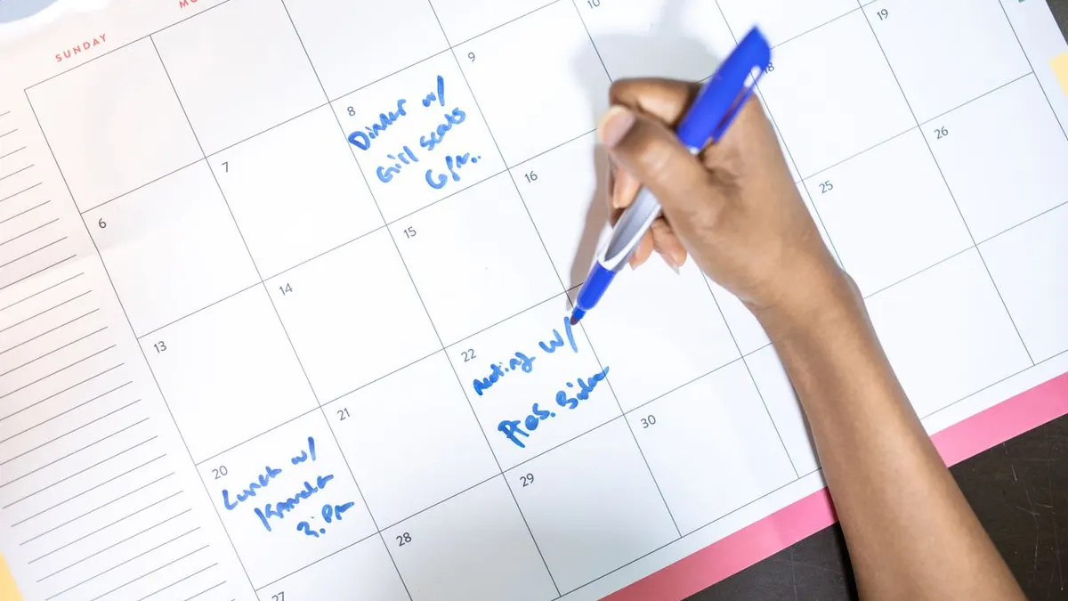 Persona escribiendo citas en un calendario con un bolígrafo azul. Vista en ángulo alto.