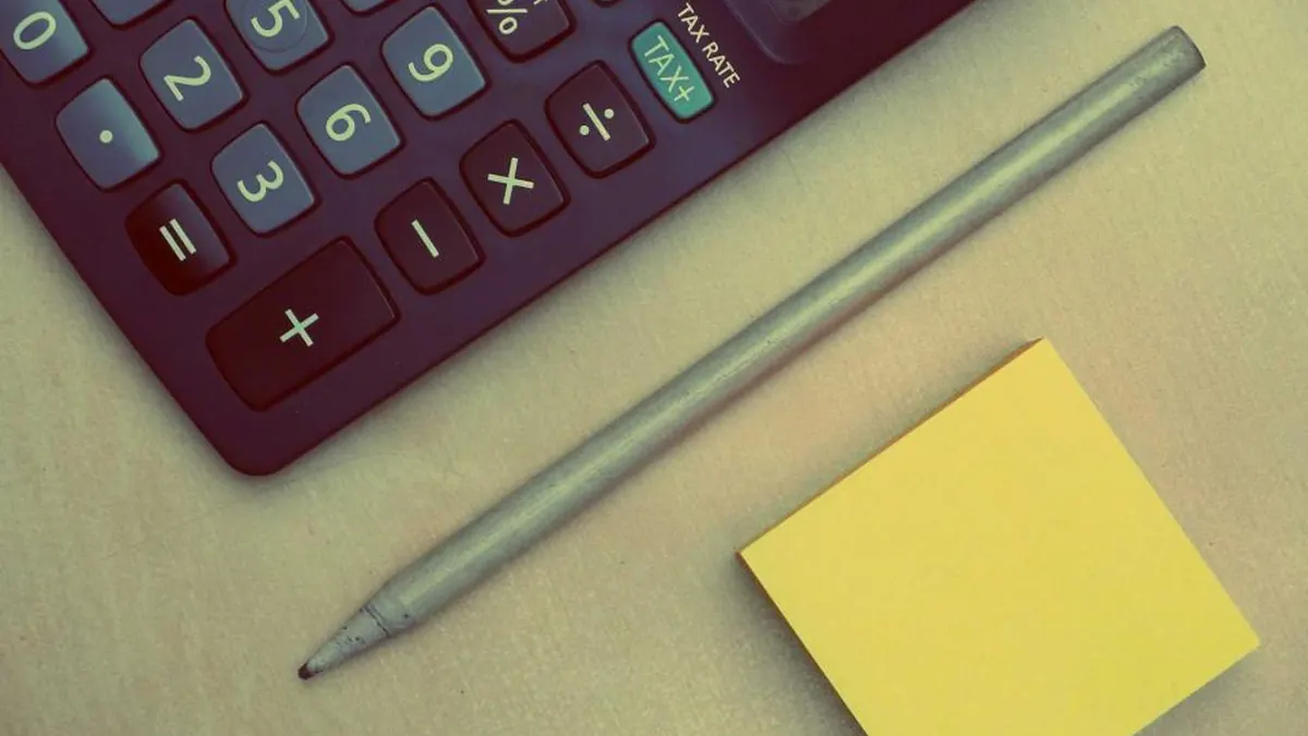 Calculadora y bolígrafo sobre una mesa con una nota adhesiva
