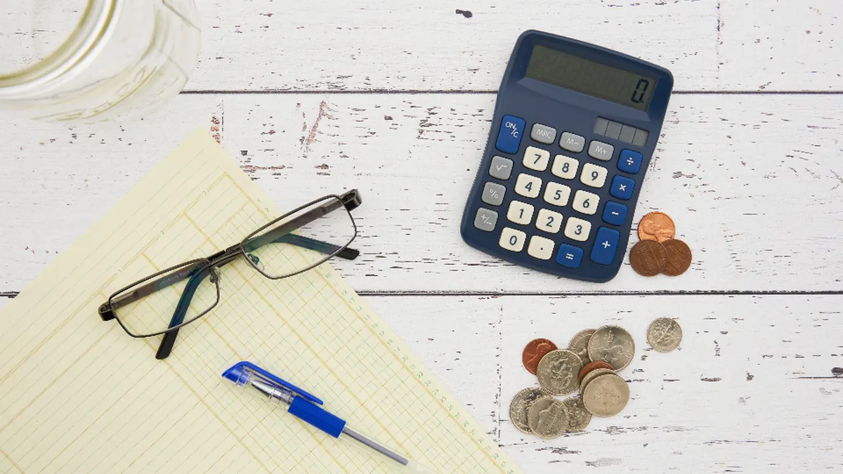 Calculadora, gafas y libreta sobre una mesa de madera blanca