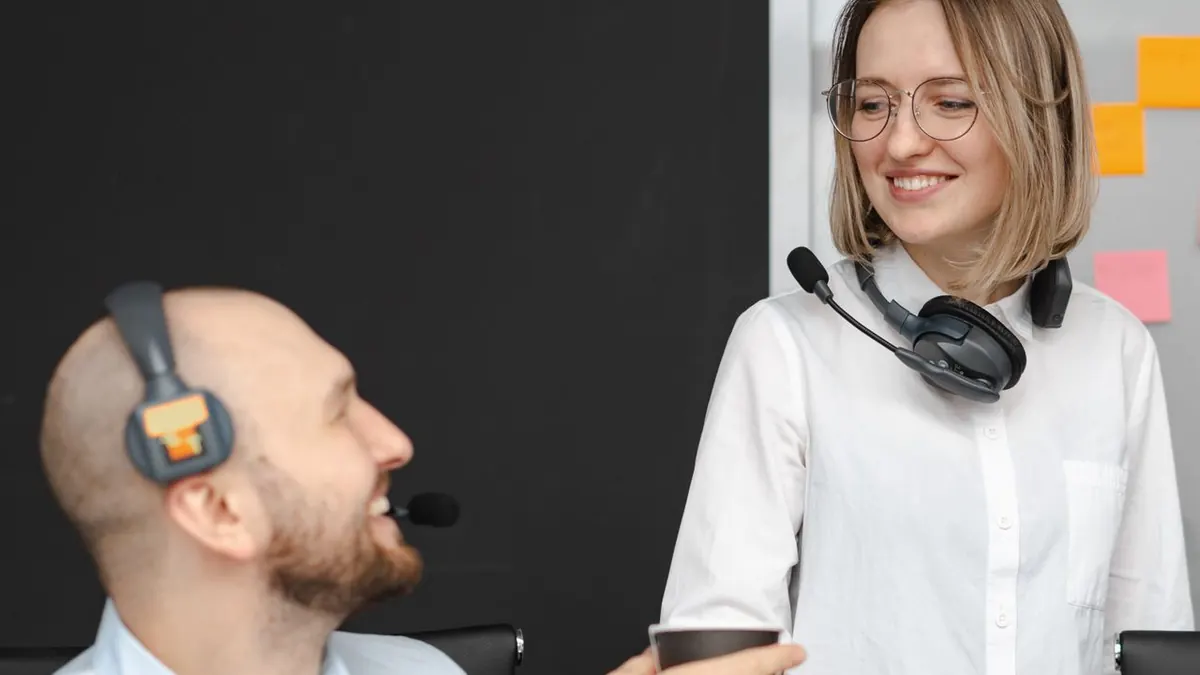 Dos colegas de centro de llamadas con auriculares sonriendo e interactuando en un entorno de oficina.