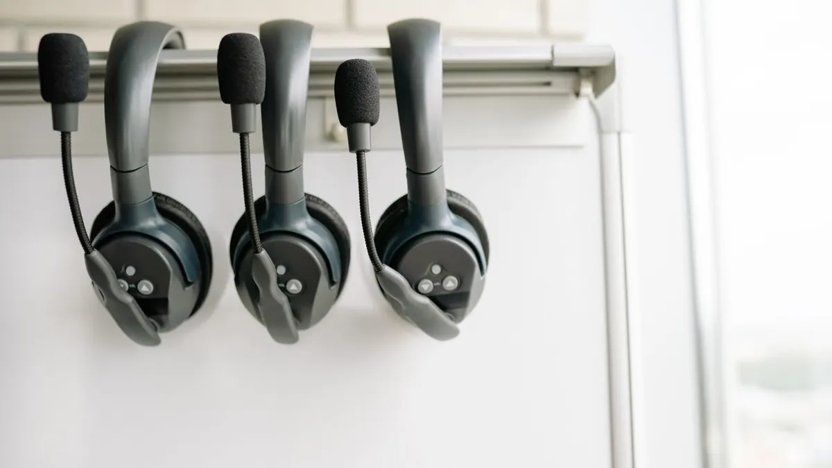 Tres auriculares negros organizados cuidadosamente en un gancho de pizarra blanca, enfatizando tecnología y comunicación.