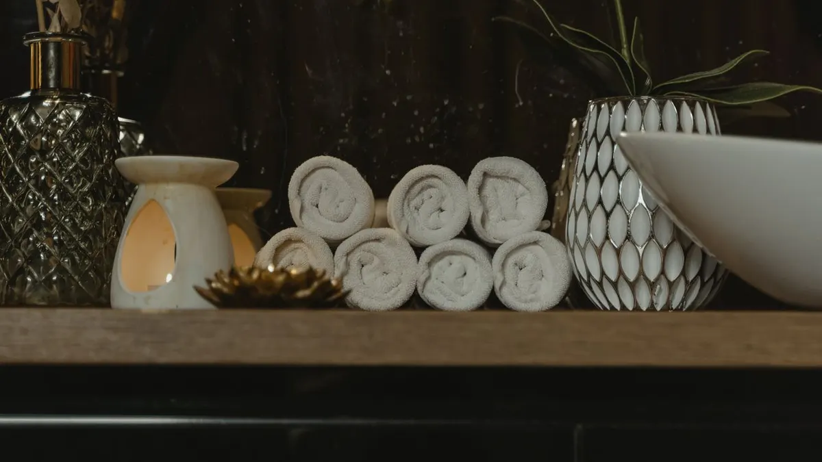 Configuración de spa serena con toallas enrolladas, luz de velas y jarrones decorativos en una estantería de madera.
