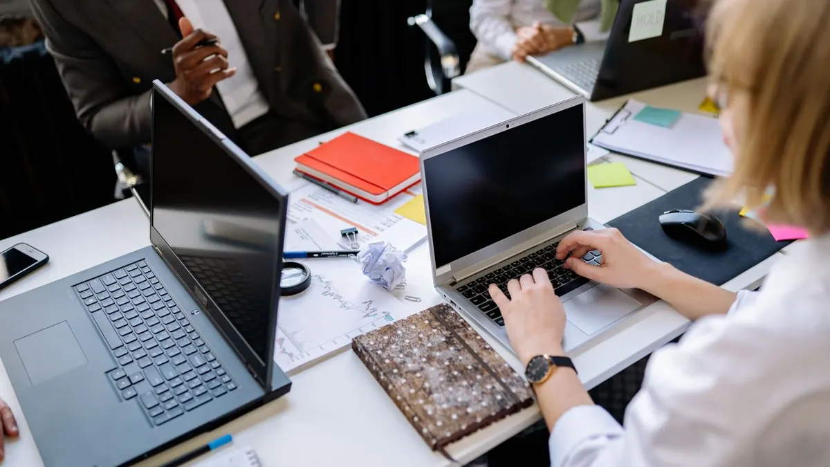 Personas discutiendo trabajo en laptops durante una reunión de equipo en un entorno de oficina moderna.