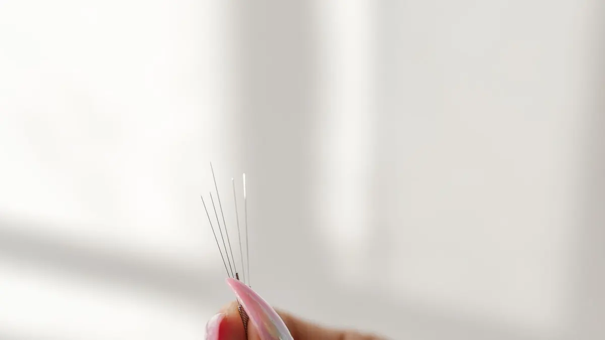Acercamiento de una mano con uñas manicurtadas sosteniendo suavemente agujas de acupuntura, simbolizando salud y belleza.