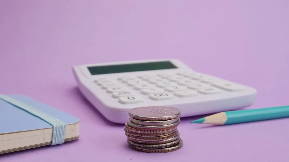 Calculadora, monedas y papelería simbolizan presupuesto y finanzas sobre un fondo púrpura pastel.