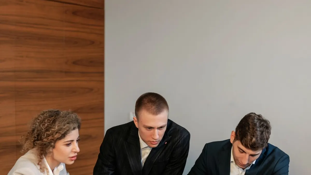 Reunión de negocios colaborativa con tres profesionales centrados en un portátil en una oficina moderna.