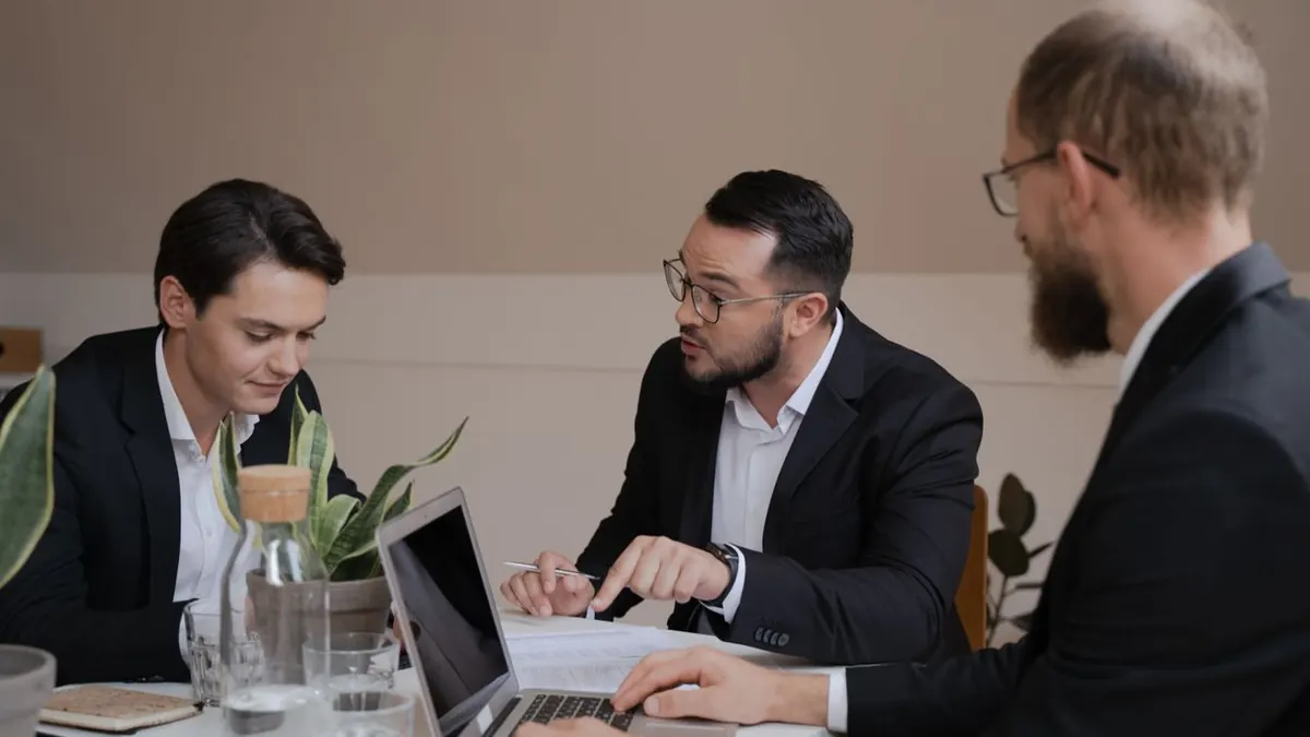 Un grupo de empresarios involucrados en una reunión, analizando informes y utilizando un portátil para su discusión.