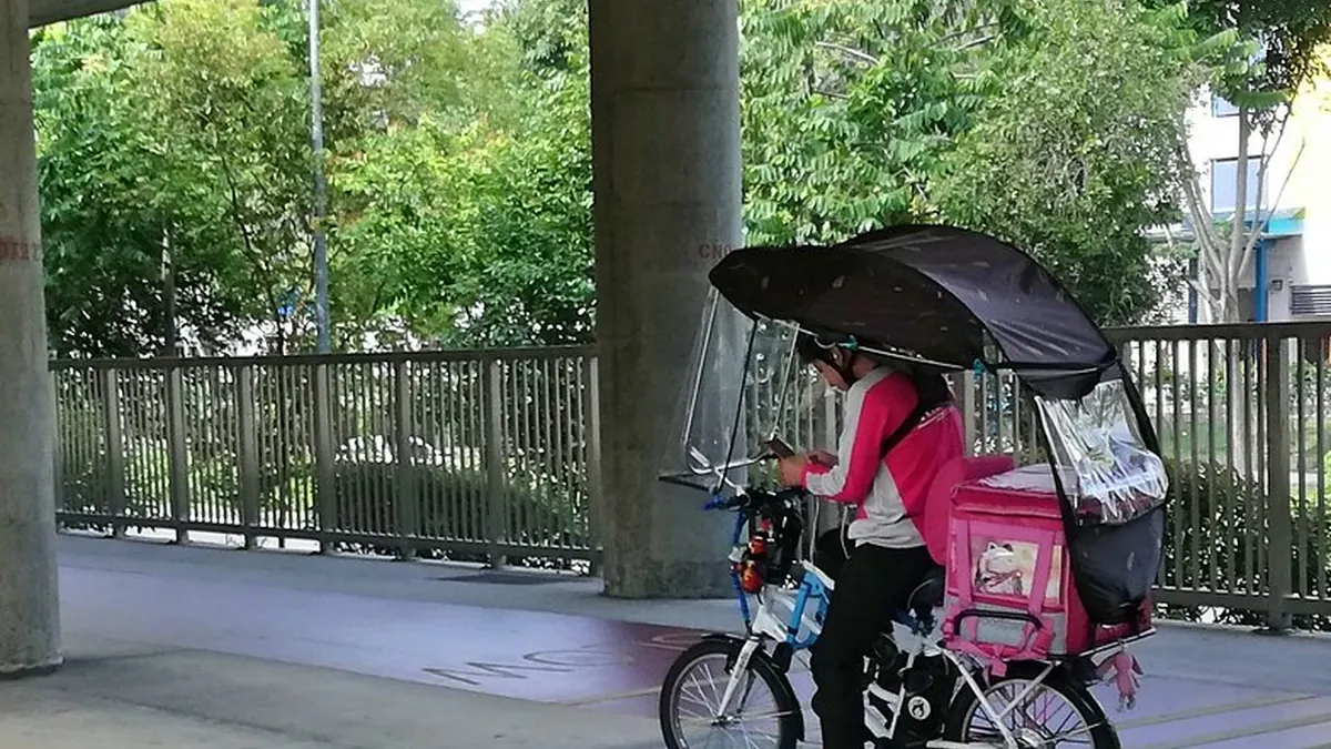Repartidora en bicicleta con una bolsa de reparto bajo un paraguas