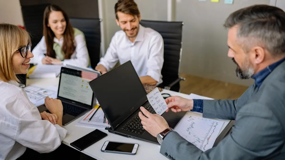 Equipo de negocios discutiendo estrategias con laptops y documentos en una mesa moderna de oficina.