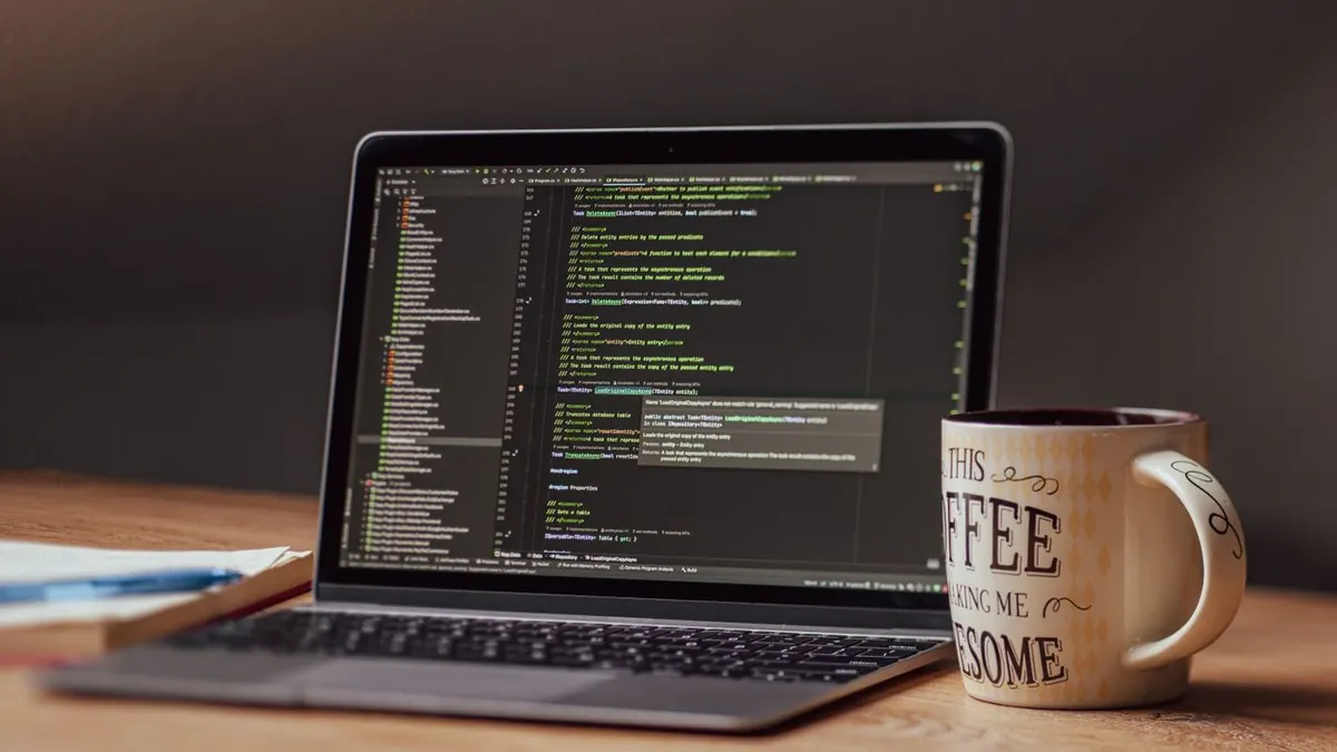 Laptop mostrando un editor de código con una taza de café en el escritorio, perfecto para temas tecnológicos.