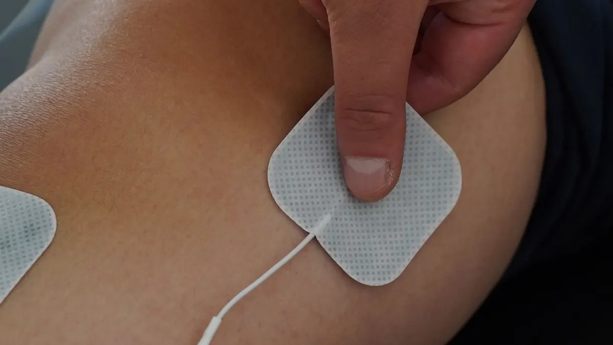 Vista en primer plano de una persona usando almohadillas de estimulación eléctrica en la rodilla para terapia.