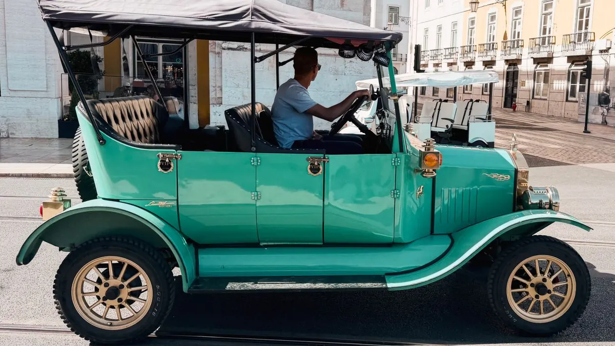Clásico coche vintage verde con un conductor en Lisboa, Portugal, a la luz del día.