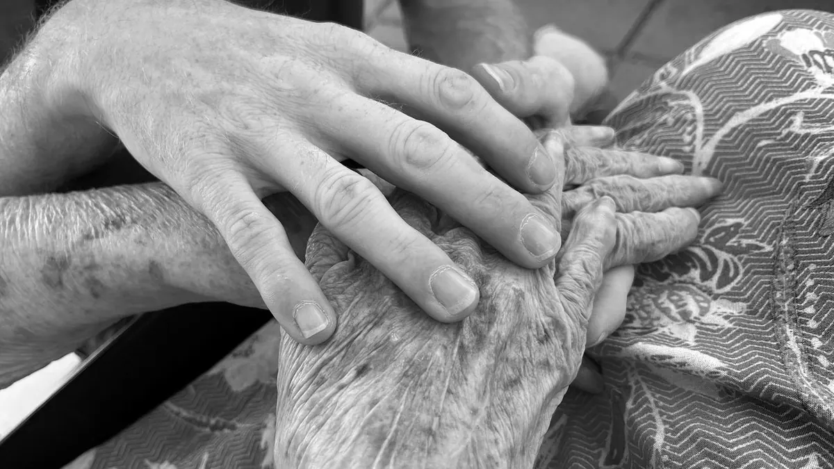 Imagen conmovedora de un adulto sosteniendo la mano de una persona mayor, simbolizando el cuidado y la conexión.
