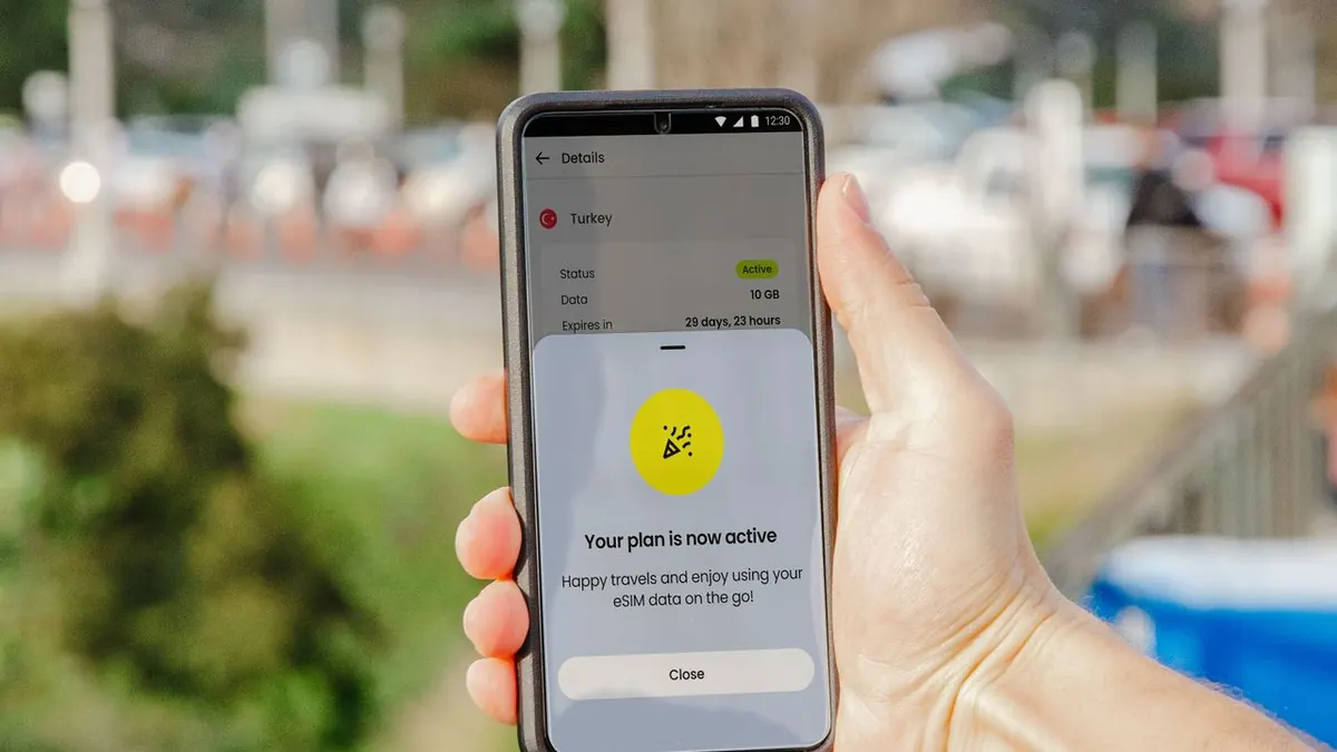 Smartphone mostrando un plan eSIM activo al aire libre, fondo de ciudad desenfocado.