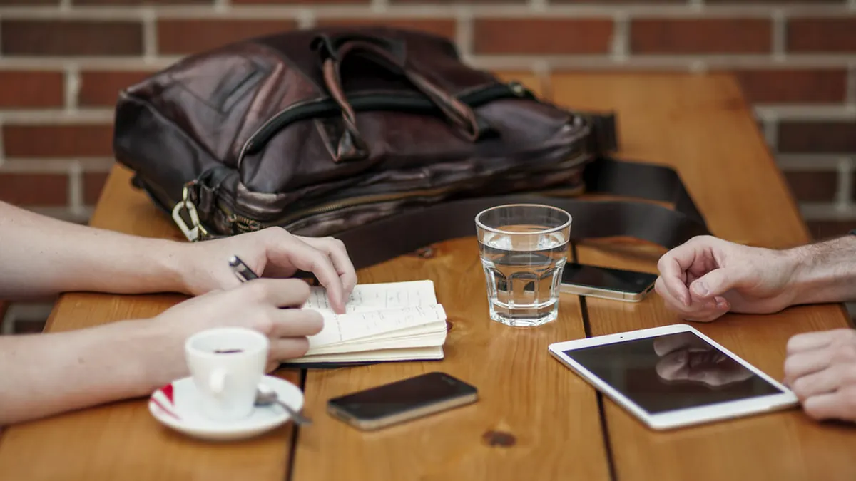 Manos sobre una mesa con una tableta y un café