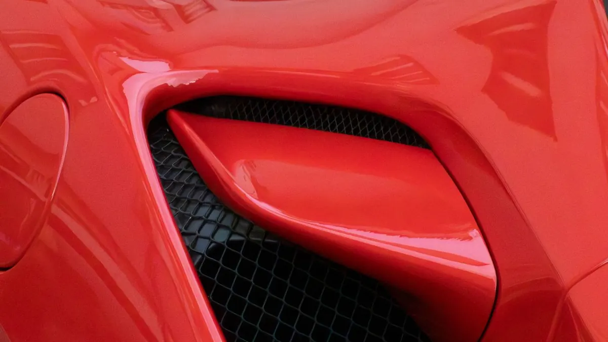 Primer plano detallado de la rejilla de ventilación de un coche deportivo rojo que muestra su diseño aerodinámico.