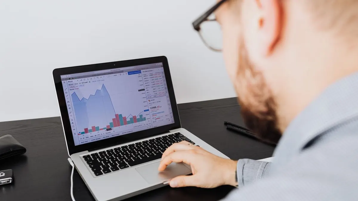 Hombre trabajando en un portátil analizando datos empresariales y gráficos financieros en interiores.